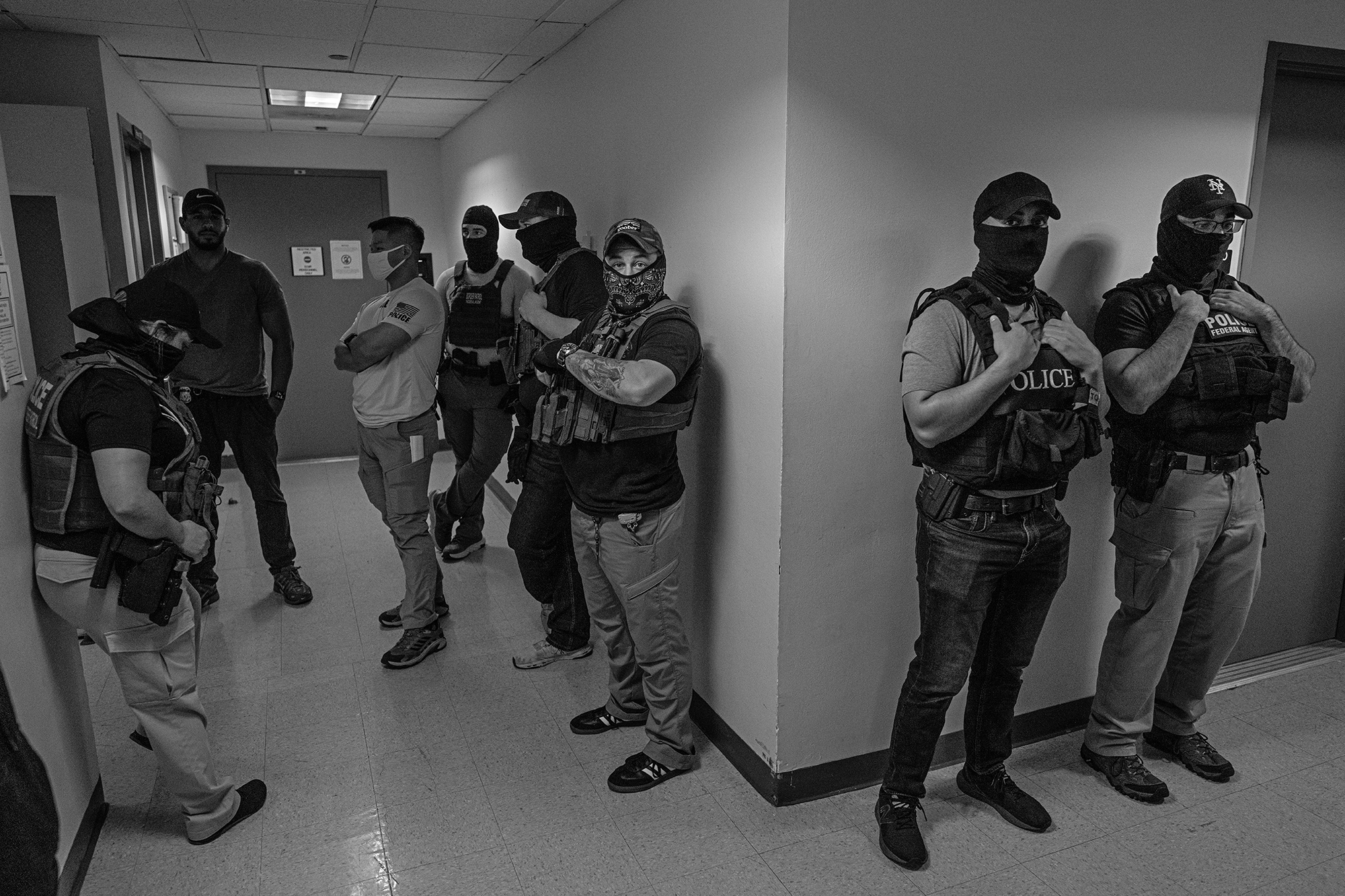 Masked Federal agents stand in a hallway outside a courtroom.
