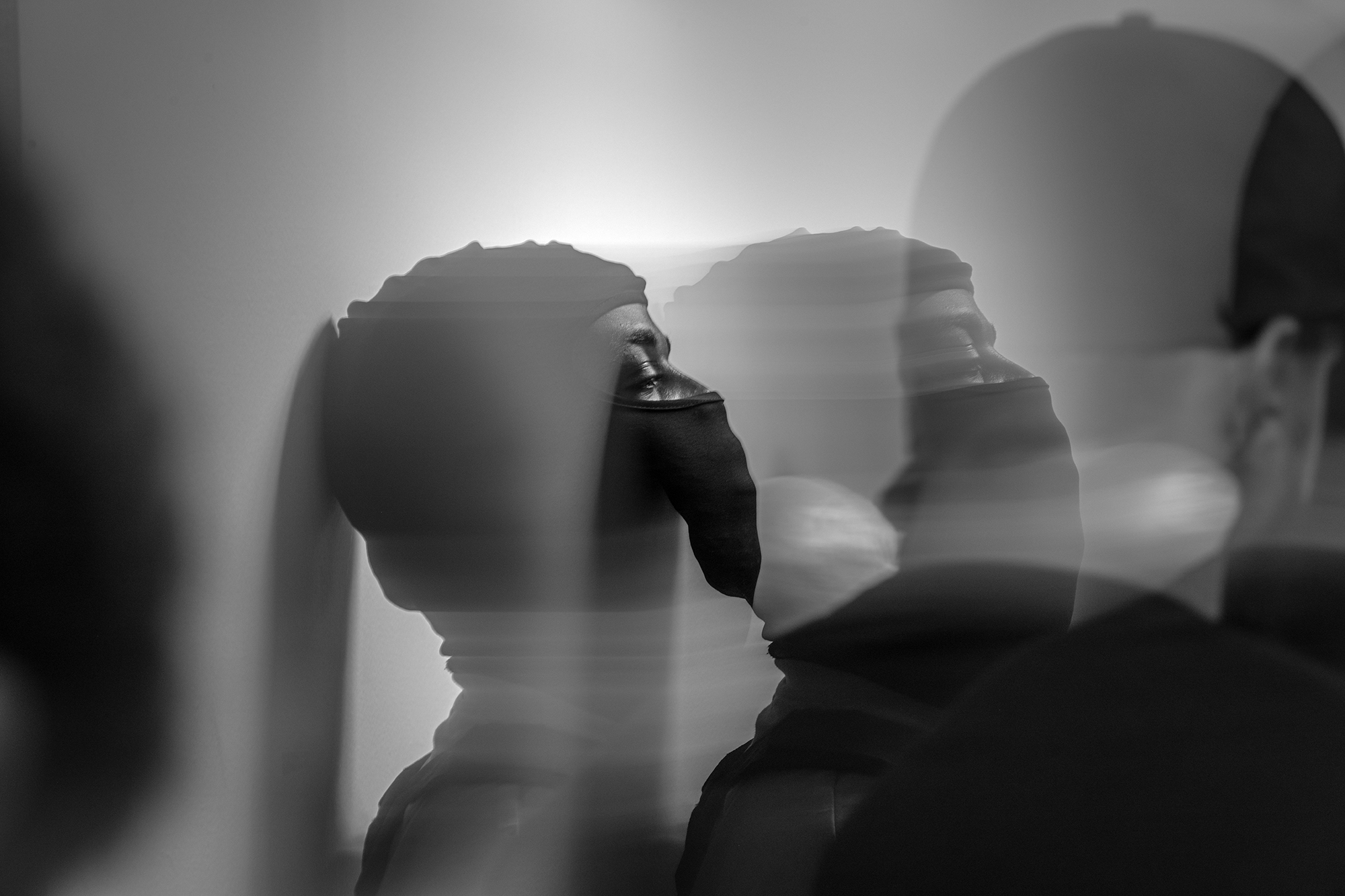 A blurred exposure of a a masked agent leaning against a wall.
