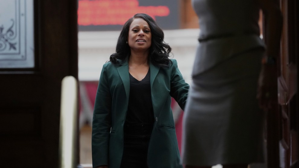 An African-American woman in a teal blazer, black shirt, and black pants standing in a doorframe in a room at the Texas State Capitol building