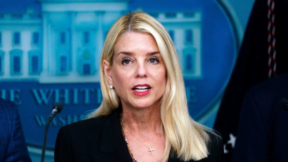 Attorney General Pam Bondi, a blonde woman wearing a cross pendant, in front of a microphone and the White House logo.