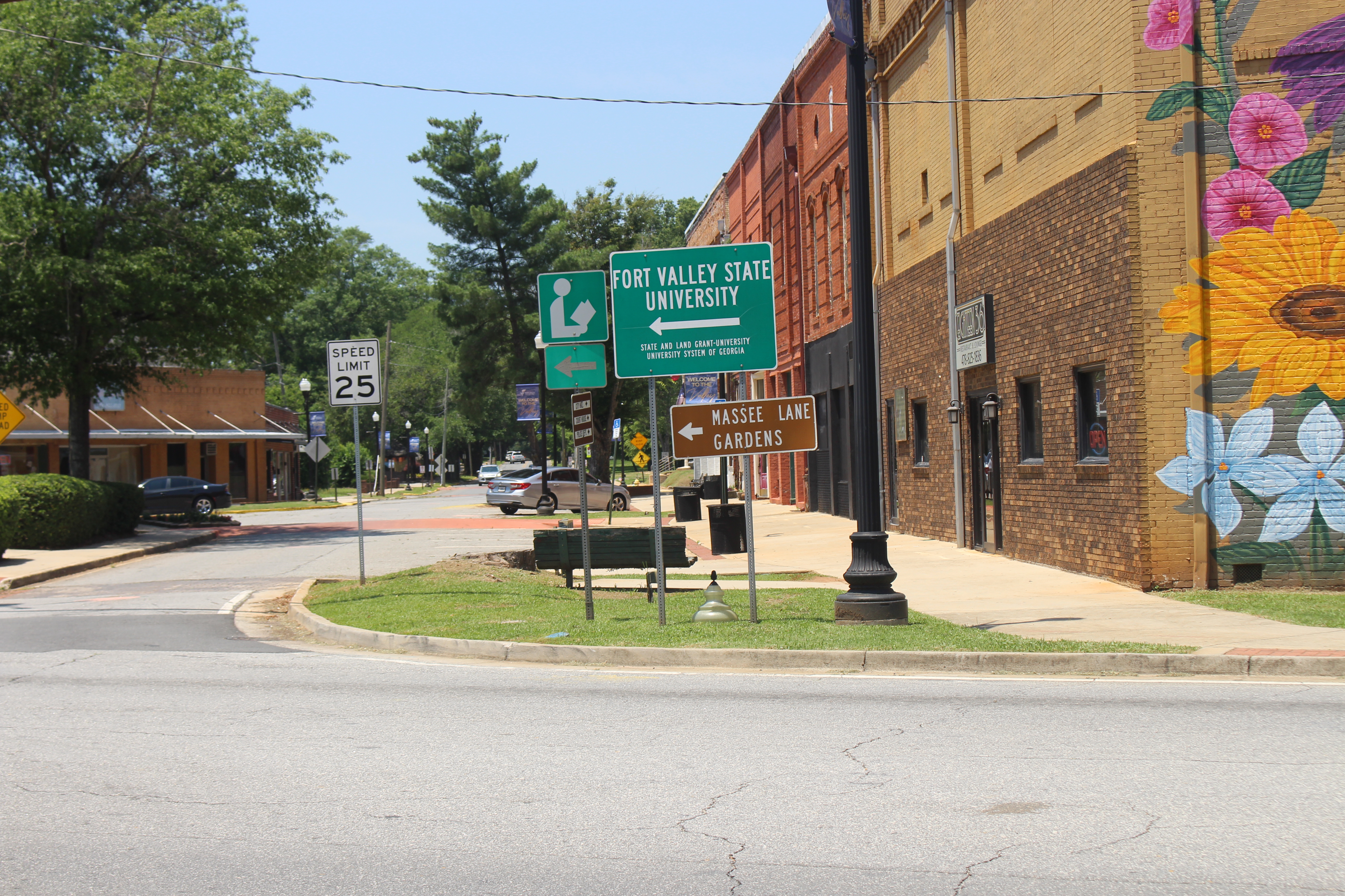 An intersection with several signs. The largest points to the left and says "Fort Valley State University." Right below it, another sign reads, "Massee Lane Gardens."