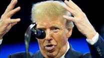 A person in a dark suit and red tie, Donald Trump, stands behind a microphone, raising both hands with palms outward while sticking out his tongue.