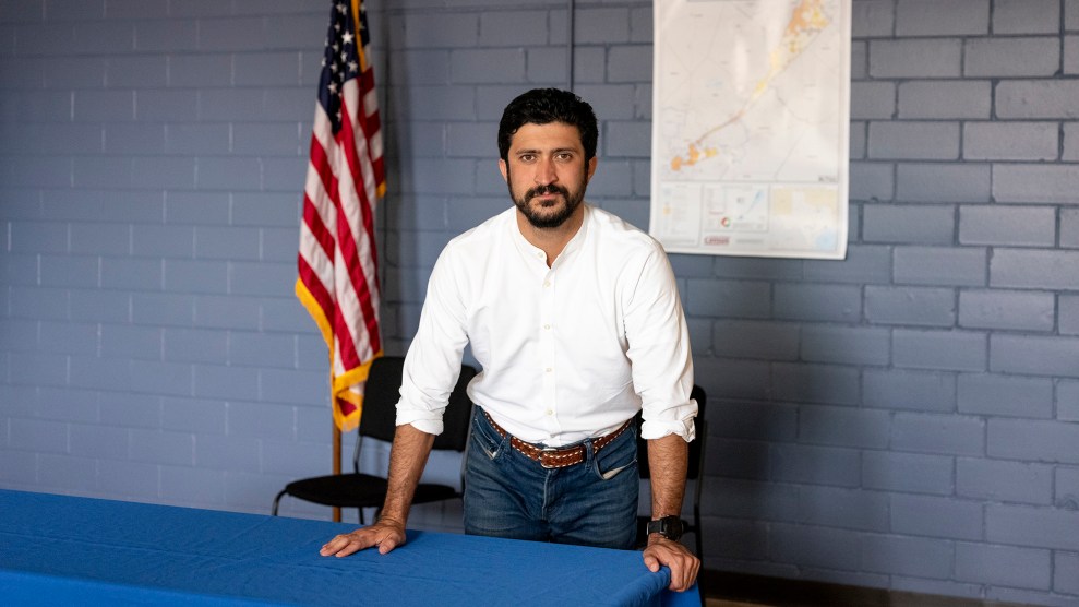 Rep. Greg Casar, in a white button down shirt and jeans, poses with an American flag in the background.