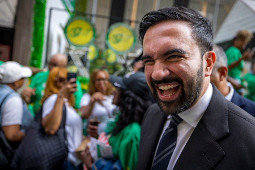 Zohran Mamdani smiles wearing a suit at a Labor Day parade.