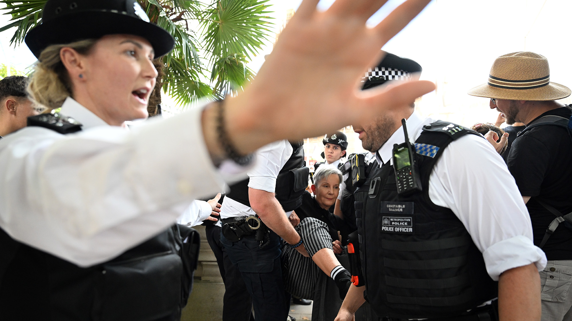 British police officer puts her hand up to try and block photographer from making image of woman getting arrested.