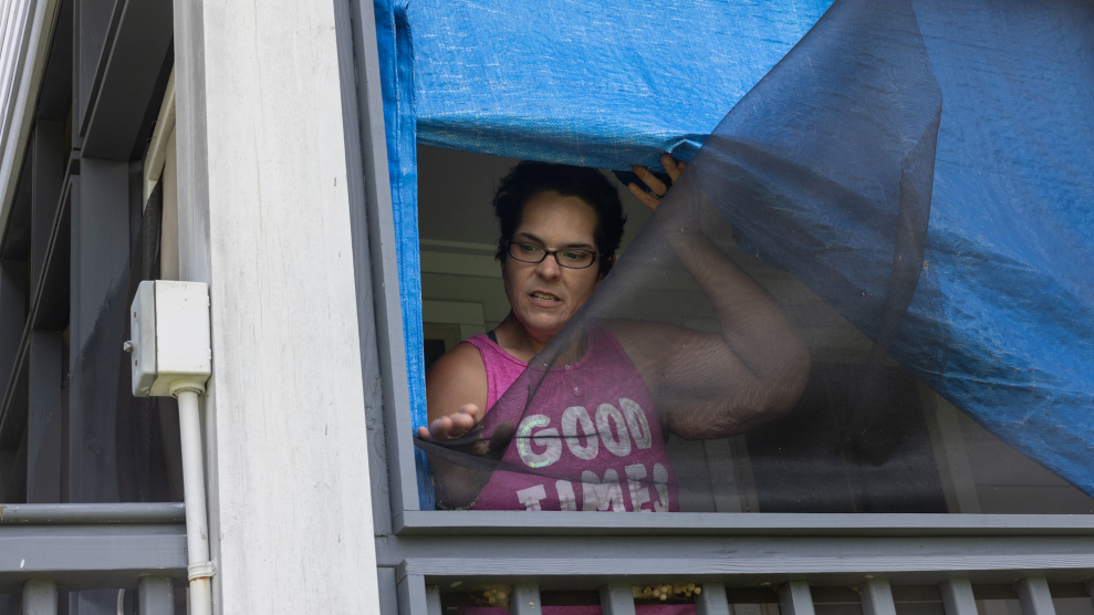 A woman looks out of a window screen that has been damaged by a storm.