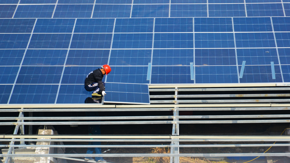 A man dressed in black wearing a red hard hat crouches as he lowers one of dozens of panels into place.