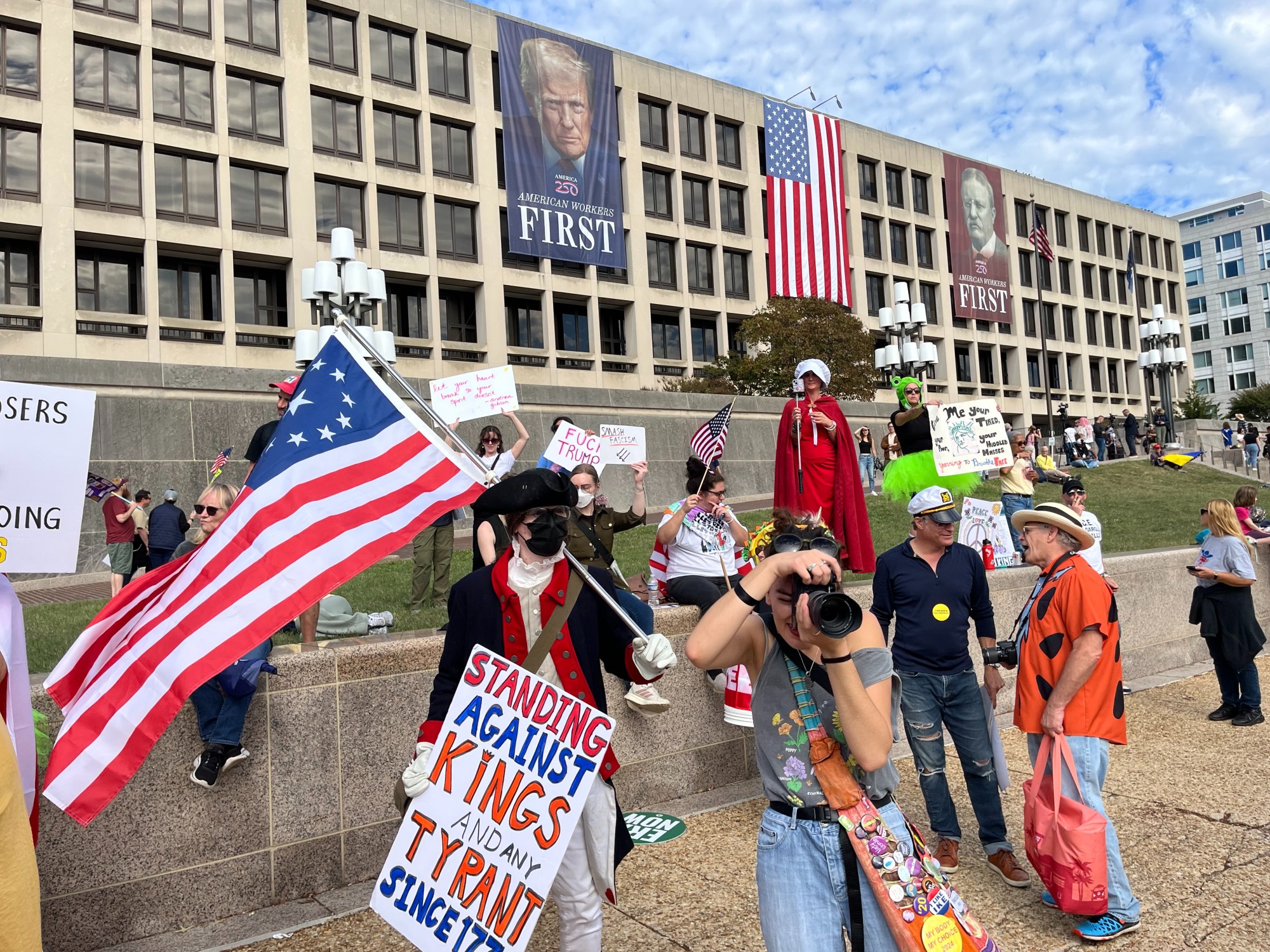 A protester in Revolutionary War garb in front of a Trump banner on the Department of Labor