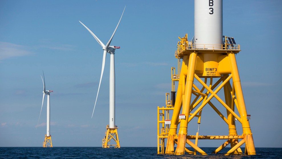 Three wind turbines in the ocean on yellow stands.