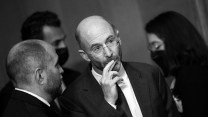 Two men talking. One man in glasses holds his hand to his mouth.