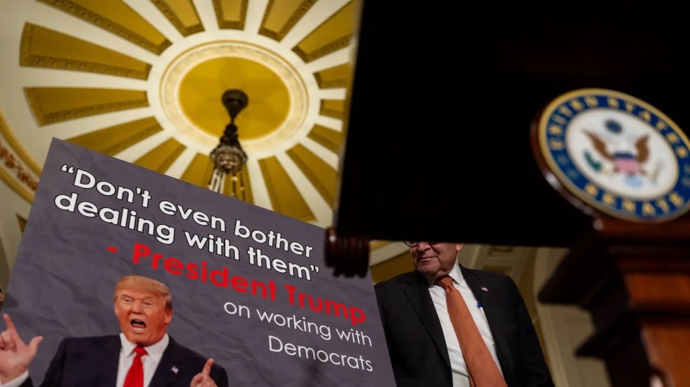 Schumer in front of a poster of Trump. The poster says " 'Don't even bother working with them,' President Trump, on working with the Democrats."