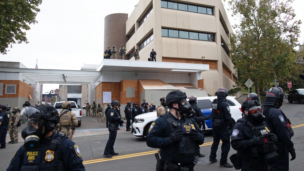 A group of masked police in Border Patrol and DHS uniforms stands outside a building complex
