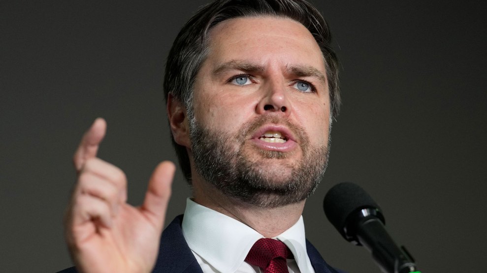 A close-up of VP JD Vance, campaigning in jacket and tie, holding up one hand to make a point.