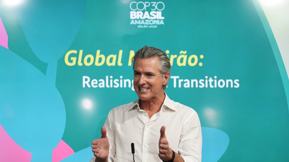 Gavin Newsom, a white man with grey hair, stands in front of a blue wall that says COP30. He holds his hands out about a foot apart and bares his teeth in emphasis.