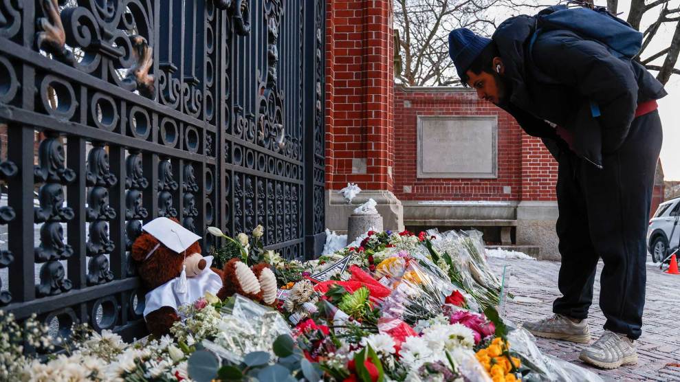 A man looks down at a huge collection of flowers and remembrances outside an iron gate