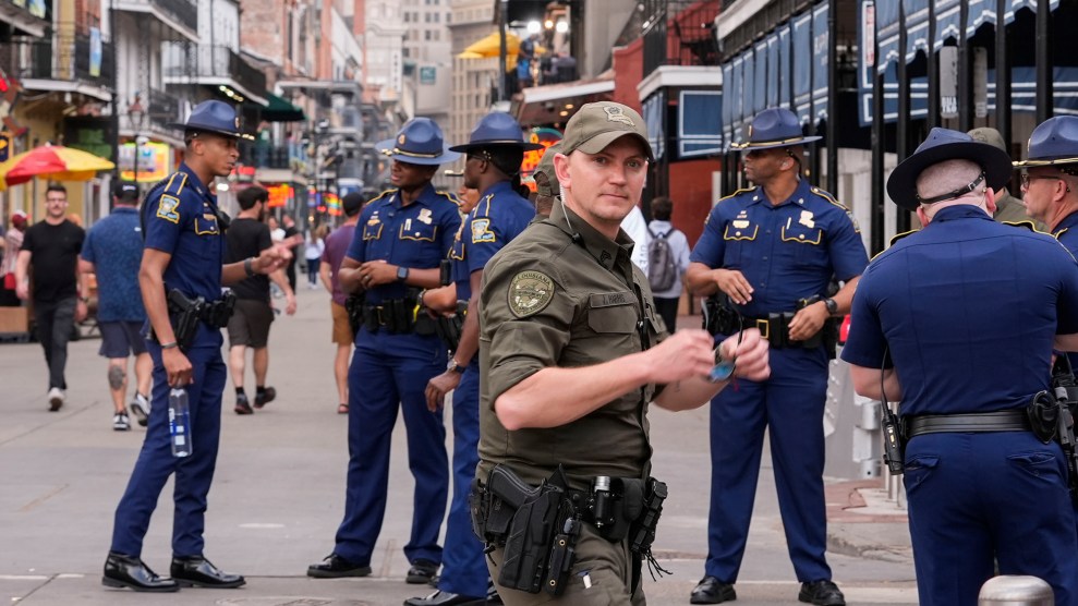 A man wearing a green uniform stands in front of men wearing blue uniforms on a busy street.