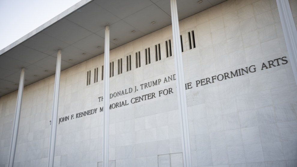 A photo of a sign on a building reading, "The Donald J. Trump and The John F. Kennedy Center For The Performing Arts" shown outside the building. The view is looking at the sign at a 45 degree angle toward the left.