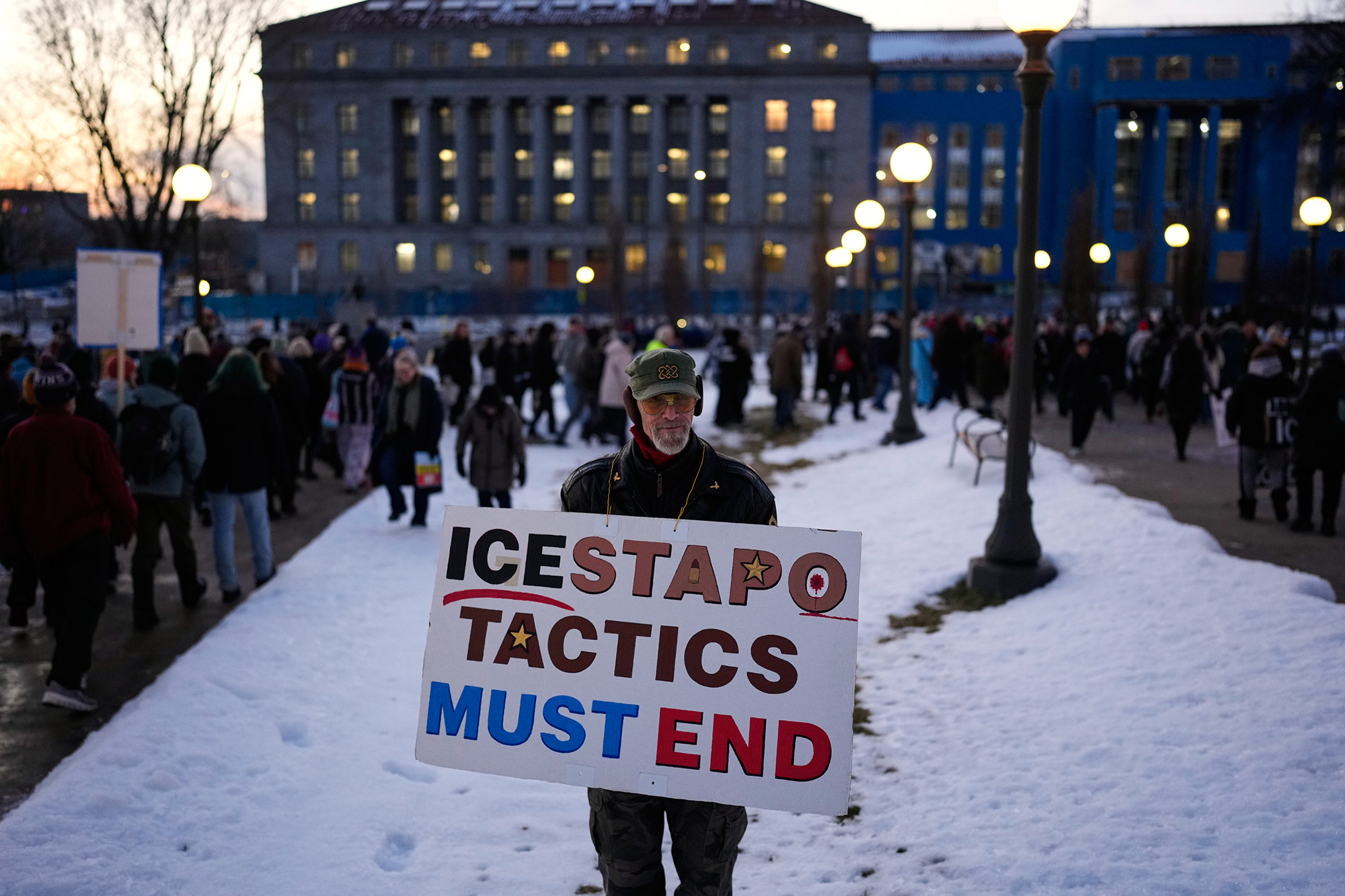 Man standing in the snow holding a sign that reads ICEStapo Tacitcs Must End"