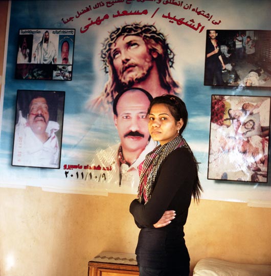 Mariam Musaad stands in front of a picture arrangement showing her father's body as it was brought to the Coptic Hospital morgue following clashes between civilians and the army near the Maspero TV building on October 9, 2011. The photographs and posters have become a permanent memory installation in Mariam's living room.