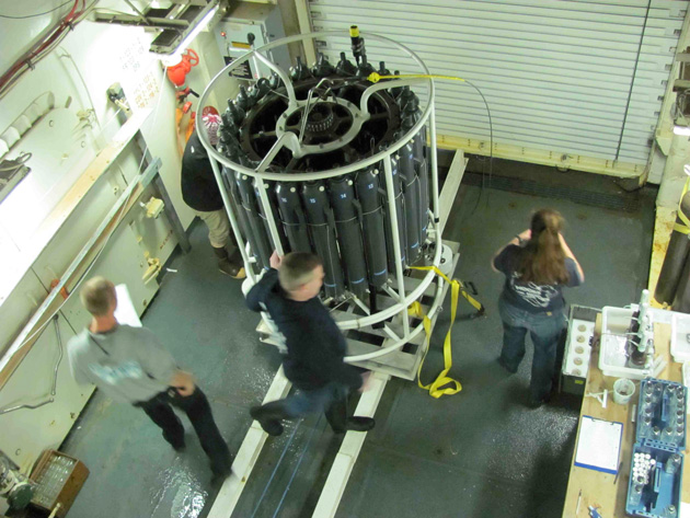 Jeremy Mathis (center) and others get ready to take samples from the CTD just brought back aboard from its trip to the bottom. Julia Whitty
